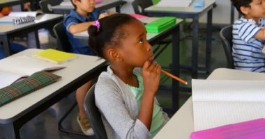 Side view of multi-ethnic school kids studying at desk in classroom at school. They are listening their teacher 4k