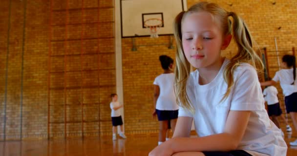 学校でバスケット ボールのコートでリラックスした白人女学生のローアングル ビュー 学童バック グラウンド でバスケの練習 — ストック動画