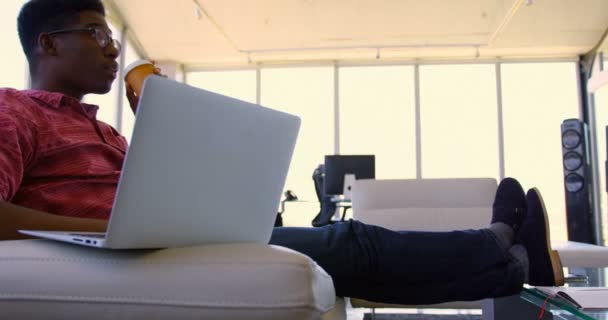 在现代办公室使用笔记本电脑的年轻英俊的非洲裔美国男性高管的侧视图 他正在喝咖啡 — 图库视频影像