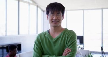 Genç yakışıklı Asya erkek yönetici duran kolları olan Önden Görünüm modern ofiste geçti. O gülümseyen ve kameraya 4 k arıyorsunuz