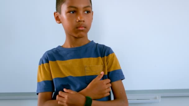 Frontansicht eines jungen afrikanisch-amerikanischen Jungen mit der Hand am Kinn, der im Klassenzimmer gegen Whiteboard steht. er denkt nach und schaut weg 4k