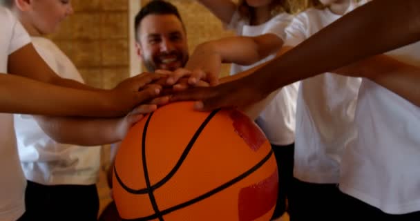 在篮球场上 年轻的高加索篮球教练和小学生组成手堆的正面观点 他们面带微笑 拿着篮球4K — 图库视频影像