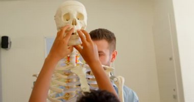 Okulda sınıfta insan iskeleti modelini tamir yetişkin Kafkas erkek öğretmenin ön görünümü. Okul çocukları ona yardım ediyor. 