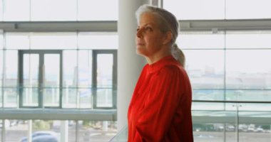 Ofis binasında duran kıdemli Kafkas iş kadınının yan görünümü. O gülümsüyor ve kamera 4k bakıyor