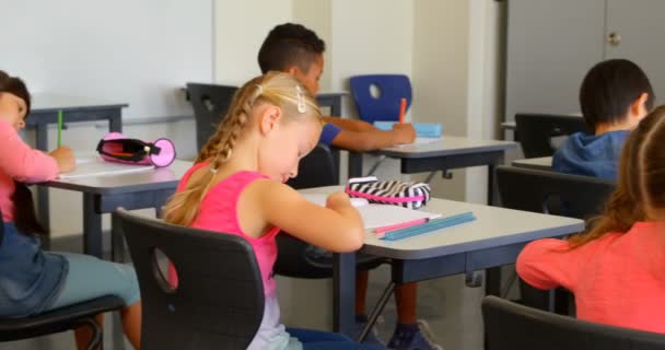 Mulit エスニック学童達の背面図学校の教室で机の上で勉強しています ノート に書いている — ストック動画
