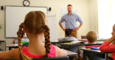 Okulda bir sınıfta masada otururken çok etnik okul çocuklarının el yetiştirmek arka görünümü. Erkek öğretmen ellerini 4k yükselterek öğrencilere işaret