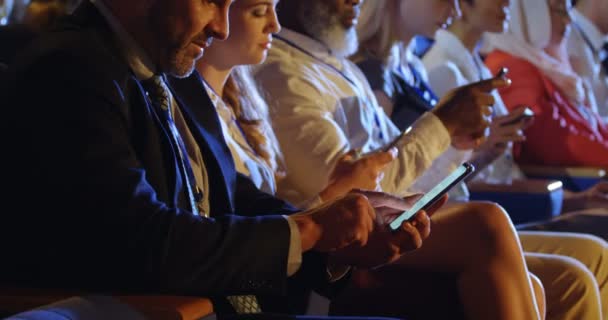 侧视图组不同的商务人士使用手机 而坐在礼堂的座位上 他们在发短信4K — 图库视频影像
