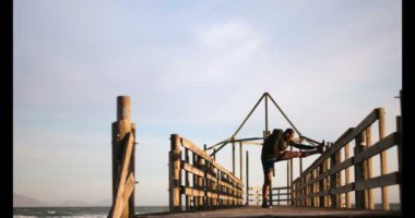 Sahilde iskelede egzersiz genç Afro-Amerikan erkek jogging yapan yan görünüm. 4 k gün ışığında esneme