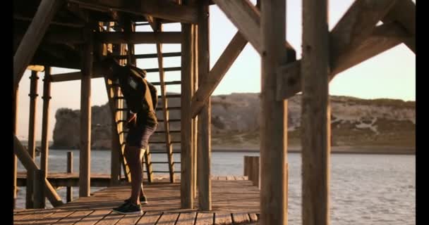 ビーチで桟橋に行使若いアフリカ系アメリカ人男性のジョガーの側面図です 日差しの中でストレッチします — ストック動画
