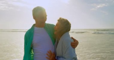 Gülümseyen ve birbirlerine güneşli bir günde 4 k kumsalda kucaklayan bir etkin üst düzey beyaz çift önden görünümü