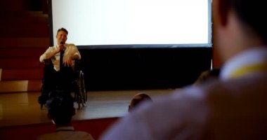 Handosme genç Kafkas engelli işadamı ön görünümü oditoryumda iş seminerinde konuşan. Tekerlekli sandalyede oturuyor. 