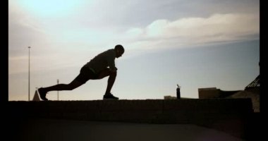 Önden Görünüm Afrikalı-Amerikalı gencin güneş altında sahilde egzersiz. 4 k germe adam silüeti