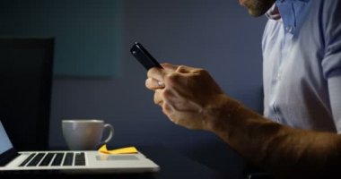 Ofiste dizüstü bilgisayar üzerinde çalışırken cep telefonu kullanarak genç Kafkas erkek yönetici yan görünümü. O gülümsüyor ve metin 4k mesaj