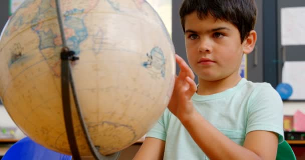 学校の教室の机で地球儀を勉強している白人の男子生徒の正面図 彼は地球4Kを見て回転しています — ストック動画