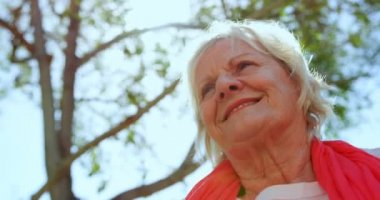 Aktif Kafkasyalı yaşlı bir kadının bakımevi bahçesinde yoga yapması düşük açı. Gülümsüyor.