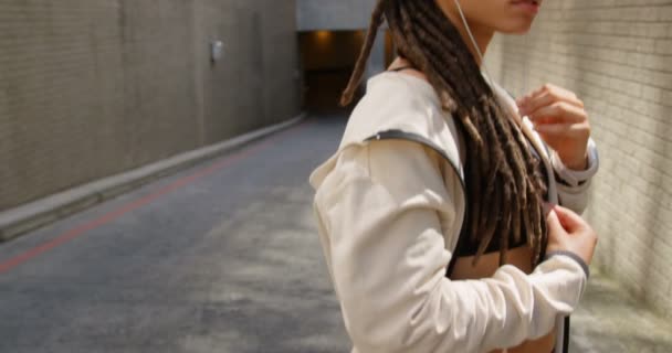 市内でイヤホンを着用している若いアフリカ系アメリカ人女性の側面図 彼女は音楽4Kを聴いています — ストック動画