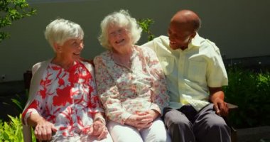 Aktif karışık ırk kıdemli arkadaşlar hemşireyurdun bahçesinde birbirleriyle etkileşim grubu. Bir bankta oturuyorlar. 