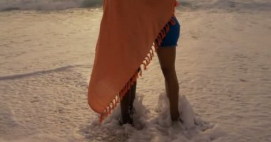 Sahilde battaniyeye sarılmış Afro-Amerikan çiftin yan görünümü. Birbirlerini kucaklıyorlar 4k