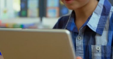Okulda sınıfta dijital tablet kullanan Kafkas öğrencinin ön görünümü. O gülümsüyor ve masa 4k oturuyor