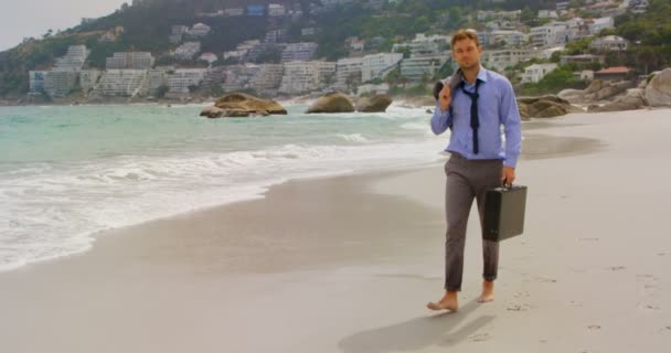 ビーチでブリーフケースを持って歩く白人ビジネスマンの正面図 彼は4Kを見ている — ストック動画