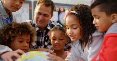 Beyaz erkek öğretmenin çocuklara sınıfta dünyayı öğrettiği ön görüş. Küreye bakıyorlar. 