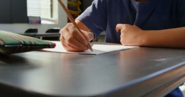 Okulda sınıfta masada okuyan özenli Asyalı öğrencinin ön görünümü. Not defterine yazıyor. 