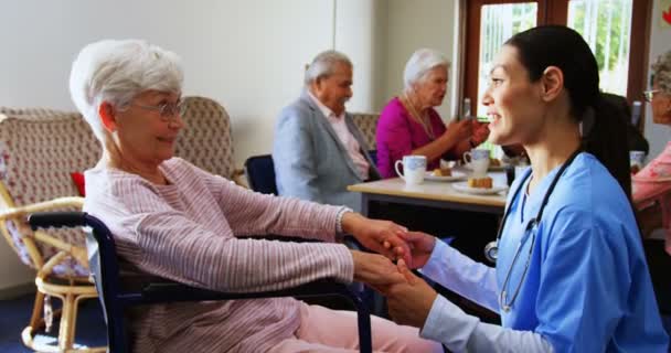 旁观的白种女医生安慰悲伤的残疾老年妇女在疗养院 资深朋友在后台互动 — 图库视频影像