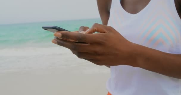 ビーチで携帯電話を使用してアフリカ系アメリカ人女性の正面図 彼女は4Kを微笑んでいる — ストック動画