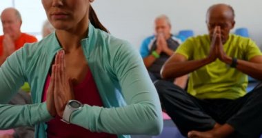 Fitness stüdyosunda yoga yapan eğitmen ile aktif karışık ırk üst düzey insanların Ön görünümü. Birlikte meditasyon yapıyorlar. 