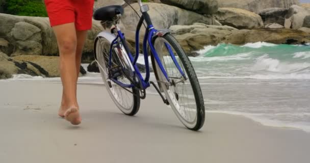 Sección Baja Hombre Caminando Con Bicicleta Playa Ondas Mar Roca — Vídeo de stock