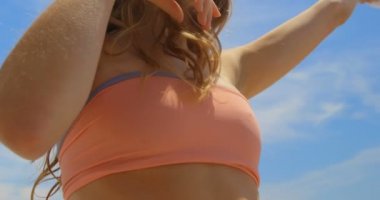 Sahilde sarong ile oynayan Beyaz kadının düşük açı görünümü. O gülümsüyor ve eğleniyor 4k