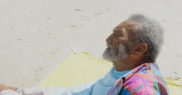 一边欣赏周到的活跃非洲裔美国老人 在阳光下在沙滩上放松 他正在看海4K — 图库视频影像