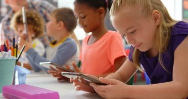 Sınıfta dijital tablet üzerinde okuyan karma ırklı okul çocuklarının yan görünümü. Erkek öğretmen arka planda öğretim okul çocukları 