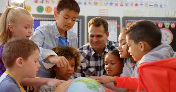 教室で地球について子供たちを教える白人男性教師の正面図 地球を見ている — ストック動画