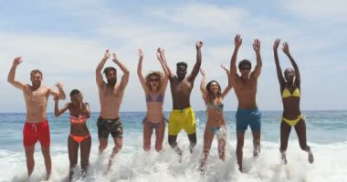 Front view of mixed-race friends jumping together on the beach. They are having fun 4k