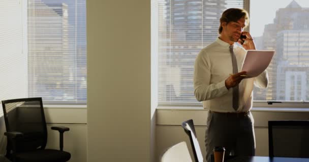 現代のオフィスで携帯電話で話す若い白人男性幹部の正面図 文書を読んでいる — ストック動画