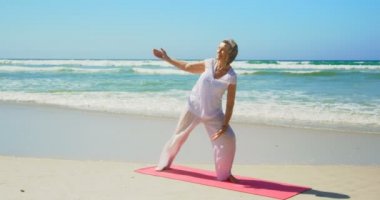 Sahilde yoga yapan aktif kıdemli Beyaz kadının ön görünümü. O güneş 4ki içinde germe olduğunu