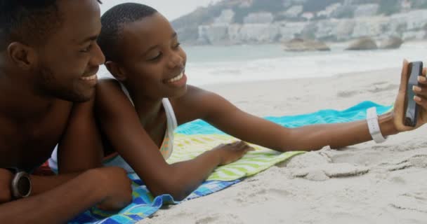 前视图的非洲裔美国夫妇采取自拍与手机在海滩上 他们在海滩上放松 — 图库视频影像