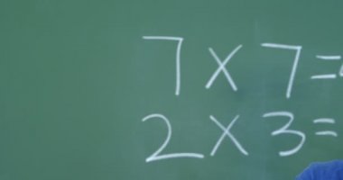 Tahtaya karşı duran ve sınıfta tebeşir gösteren Asyalı öğrencinin ön görünümü. O gülümsüyor ve kamera 4k bakıyor