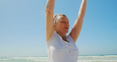 Sahilde yoga yapan aktif kıdemli Beyaz kadının ön görünümü. O gözleri kapalı 4k ile meditasyon olduğunu
