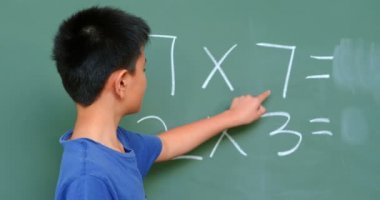 Asyalı öğrencinin okulda ki sınıfta tebeşir tahtasında matematik problemini çözmesinin arka görünümü. O çarpma 4k yapıyor