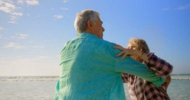 Sahilde dans eden aktif kıdemli Kafkas çiftinin yan görünümü. El ele tutuşuyorlar 4k