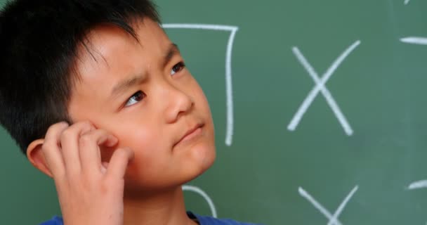 在教室里 有思想的亚洲学生把头撞在黑板上 他看着远方 — 图库视频影像