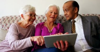 Aktif karışık ırk kıdemli arkadaşlar hemşireevinde dijital tablet üzerinden tartışıyor grup. Kanepede oturuyorlar. 