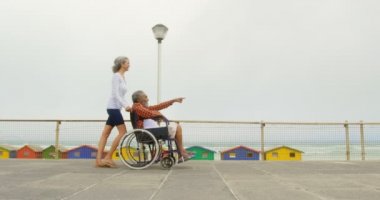 Aktif üst düzey Afro-Amerikan kadın gezinti tekerlekli sandalyede engelli adam iterek yan görünümü. Kıdemli adam işaret ve onu 4k gösteren