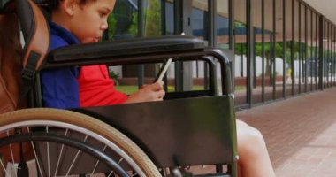 Okul koridorunda dijital tablet kullanarak engelli Afro-Amerikan öğrenci yan görünümü. Tekerlekli sandalye4k'te oturuyor.