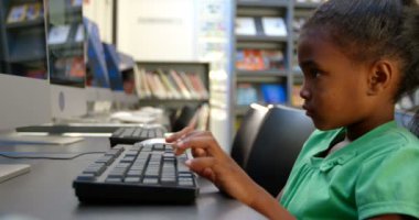 Okuldaki kütüphanede bilgisayar kullanan Afro-Amerikan kız öğrencinin yan görünümü. O masa 4k oturuyor