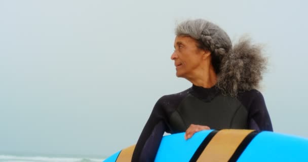 活跃高级非洲裔美国女冲浪者的正面景色 冲浪板矗立在沙滩上 她看着远方4K — 图库视频影像