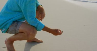 Sahilde deniz kabuğu tutan aktif kıdemli Kafkasyalı adamın yan görünümü. 4k