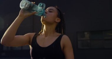 Şehirde su içen genç Afro-Amerikan kadının ön görünümü. O yorgun ve yorgun 4k